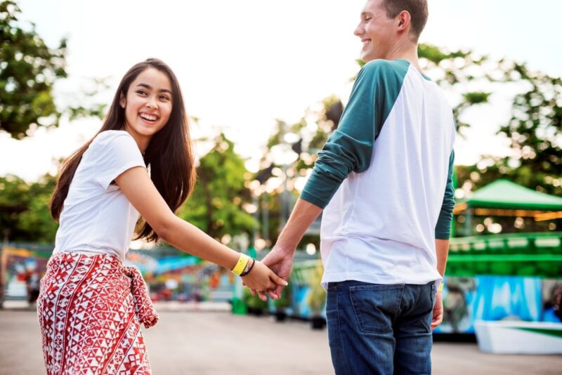Two young adults holding hands and smiling while walking outdoors, representing supportive relationships and social connection for autistic adults.