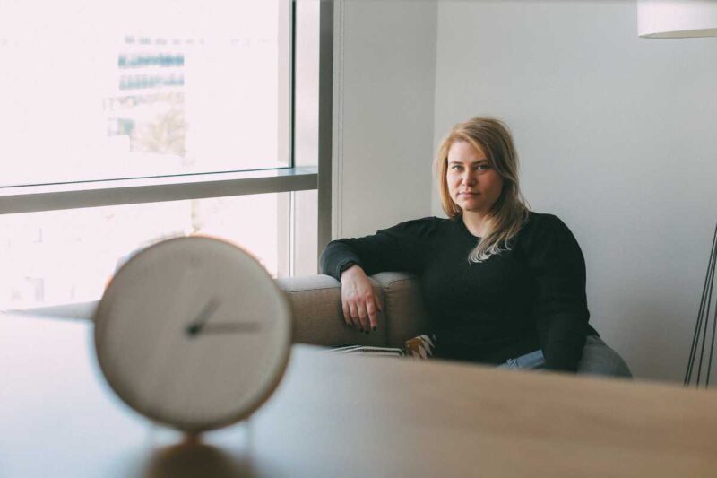 Woman sitting thoughtfully beside a window with a clock in the foreground, representing different experiences of time